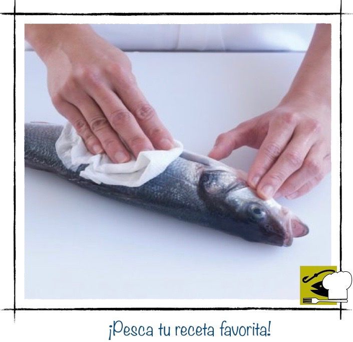 Una persona secando un pescado entero y limpio de escamas, con papel absorbente después de haberlo enjuagado.