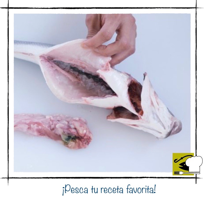 Una persona retirando con la mano las vísceras del interior de un pescado ya abierto, con los intestinos sobre la tabla de cortar.