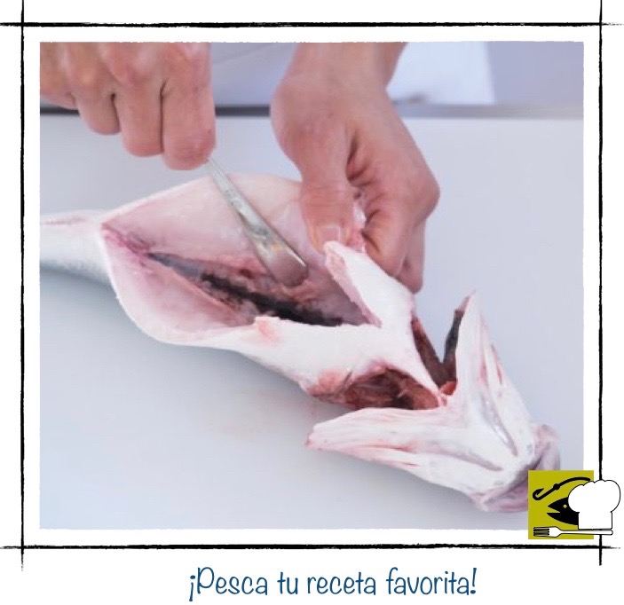 Una persona usando la punta de una cuchara para raspar y limpiar la línea de sangre oscura que se encuentra pegada a la espina central del pescado.