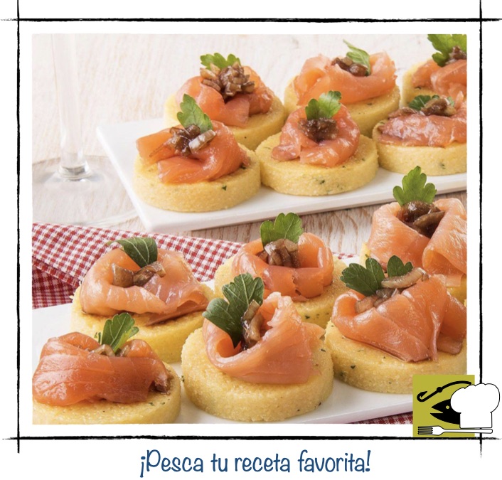 Crostini de polenta redondos con láminas de salmón ahumado y hierbas frescas.
