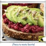 Tosta de hummus de remolacha rojo con laminas de aguacate y semillas variadas.
