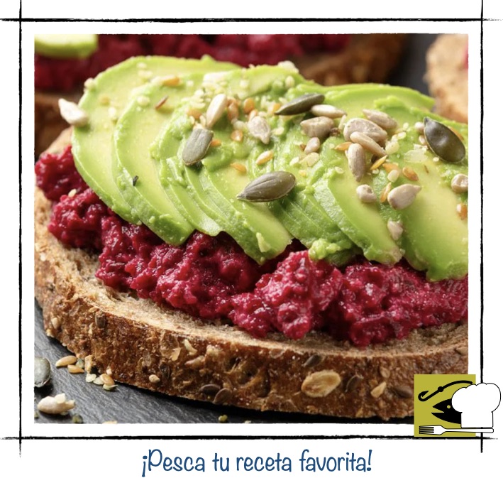 Tosta de hummus de remolacha rojo con laminas de aguacate y semillas variadas.